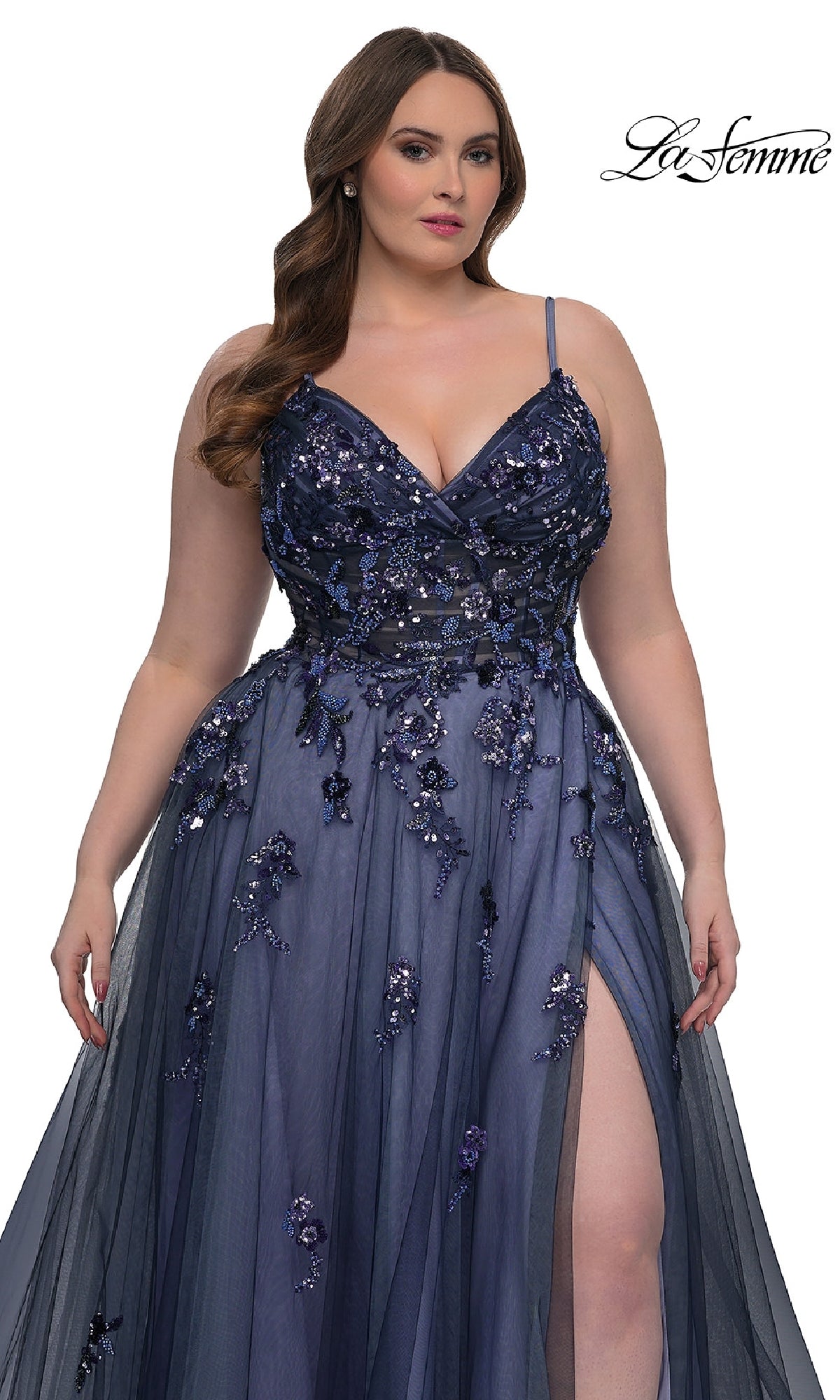A woman in the Navy Plus-Size Prom Dress: La Femme 33061 stands against a white background. The dark blue gown has thin straps, a high slit, sequin beaded floral appliqué, and an elegant A-line skirt.